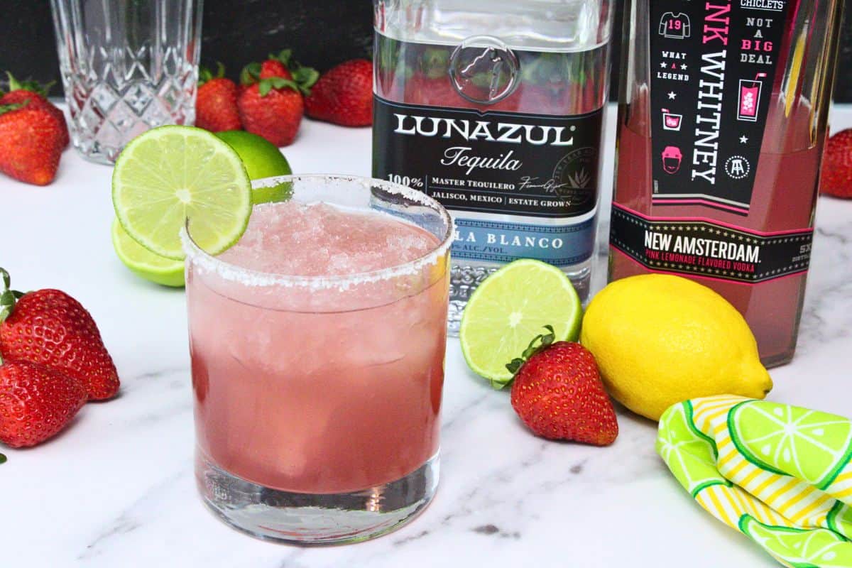 pink whitney margarita with salt rim and lime wheel in front of tequila and pink whitney bottle