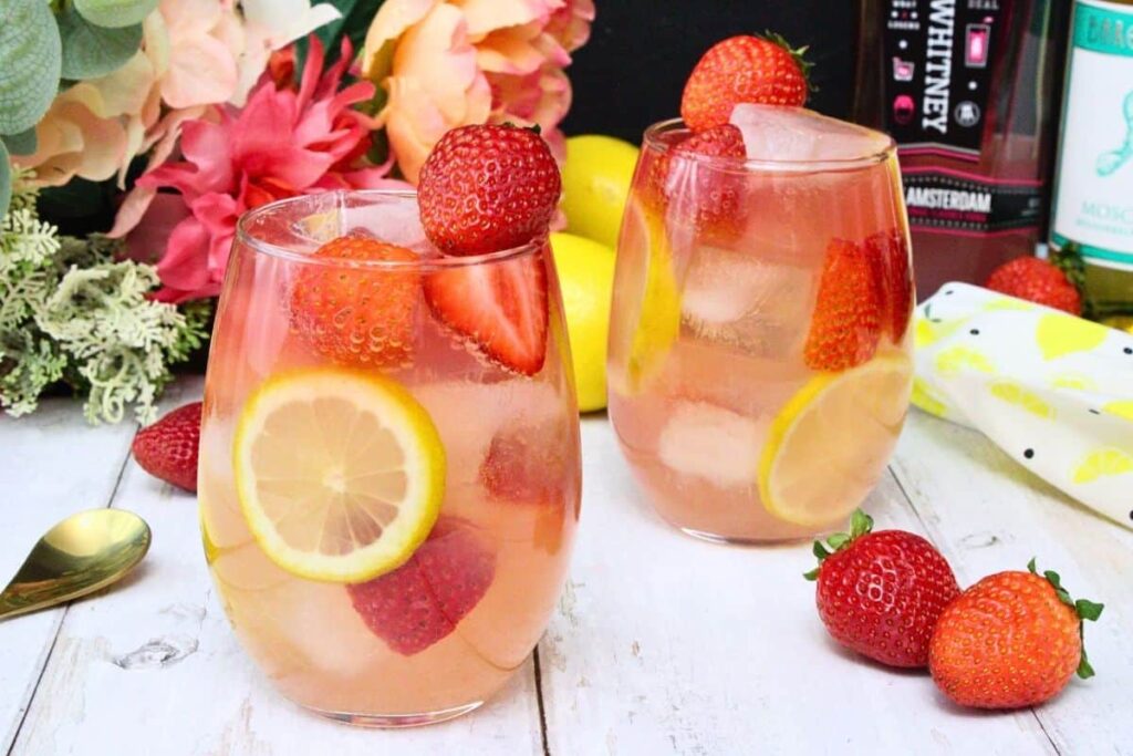 two giggle juice drinks filled with fresh strawberries and lemon on a white wooden table