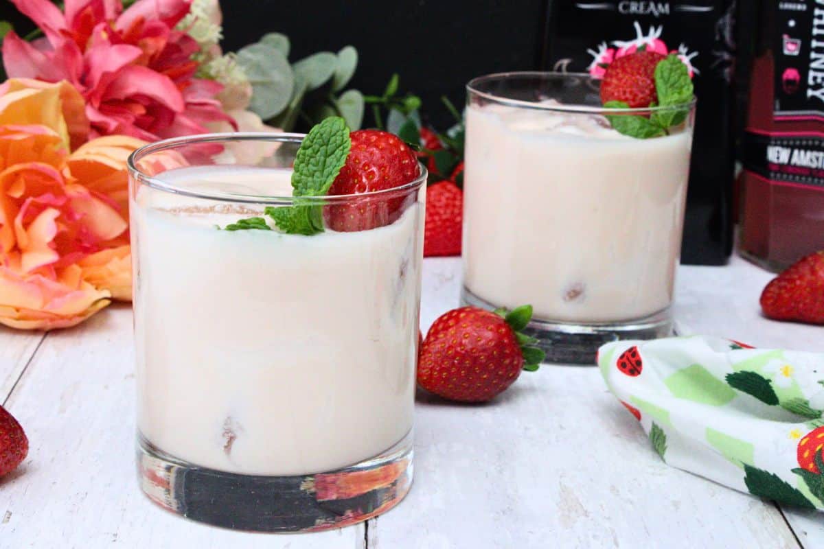 two pink russian cocktails garnished with fresh strawberry and mint leaf surrounded by more fruit and flowers