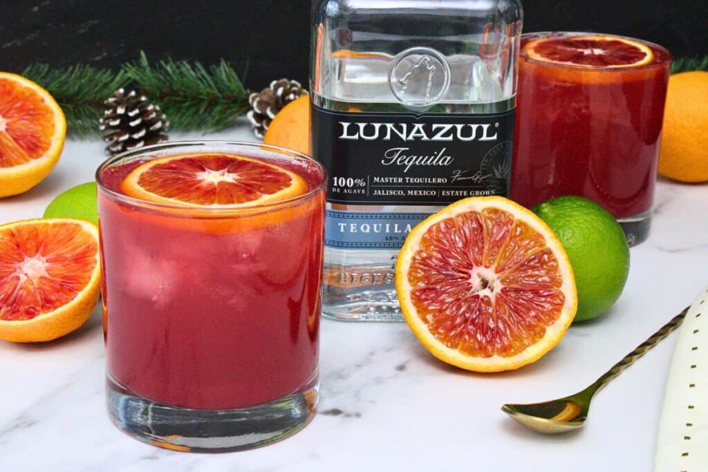 blood orange paloma with blood orange slice garnish in front of tequila bottle