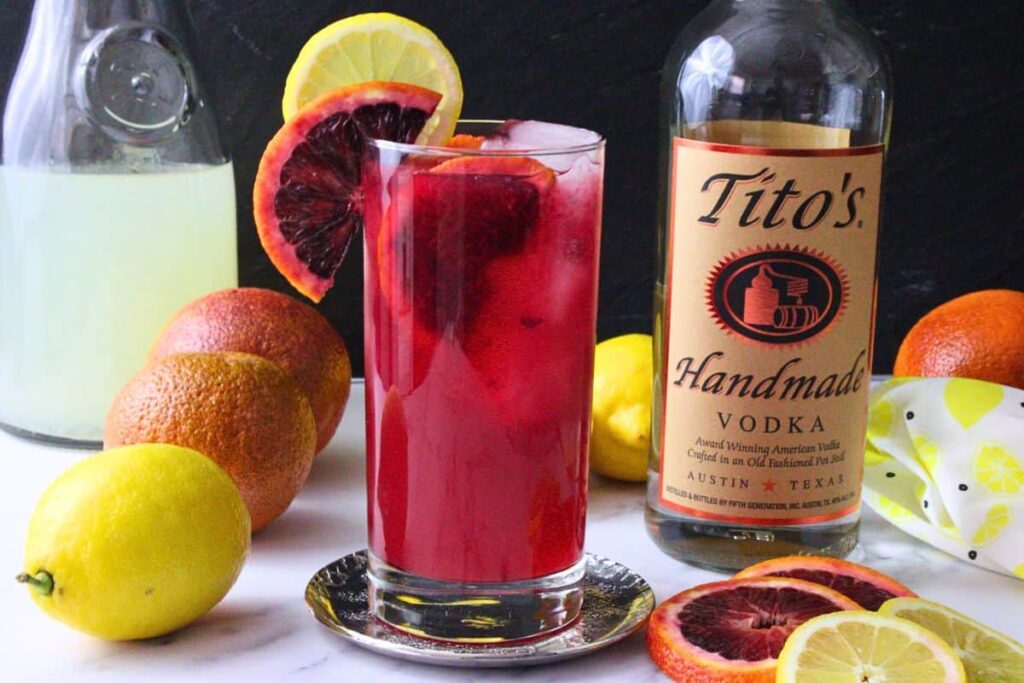 blood orange vodka lemonade drink garnished with blood orange and lemon next to vodka bottle