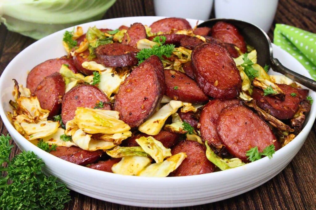 closeup view of a white bowl filled with cabbage and sausage plus a serving spoon in the back