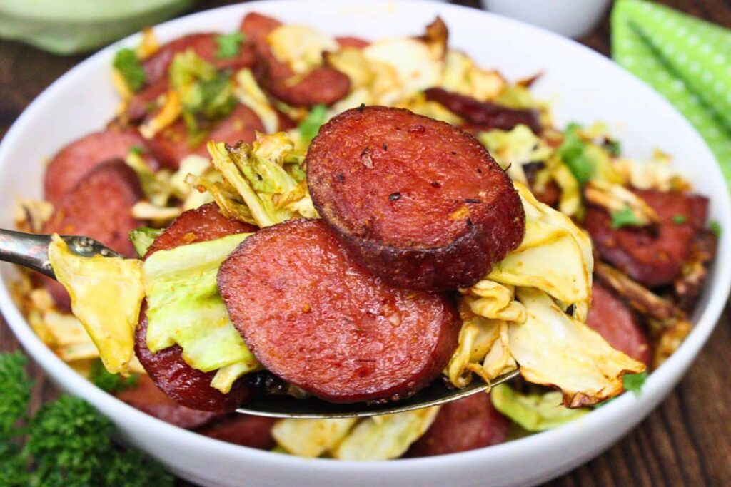 holding up a serving spoon filled with cabbage and sausage over the bowl