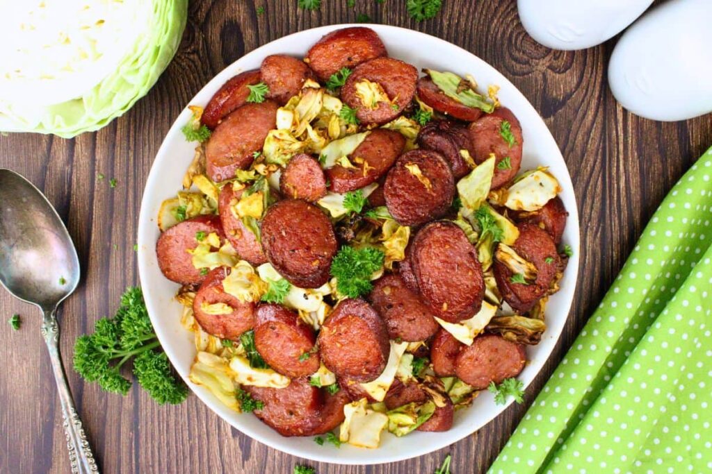 overhead view of cabbage and sausage in a white bowl with a serving spoon and head of cabbage off to the side