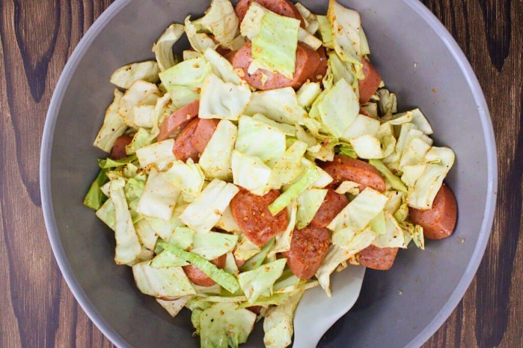toss cabbage and sausage in a bowl with seasonings