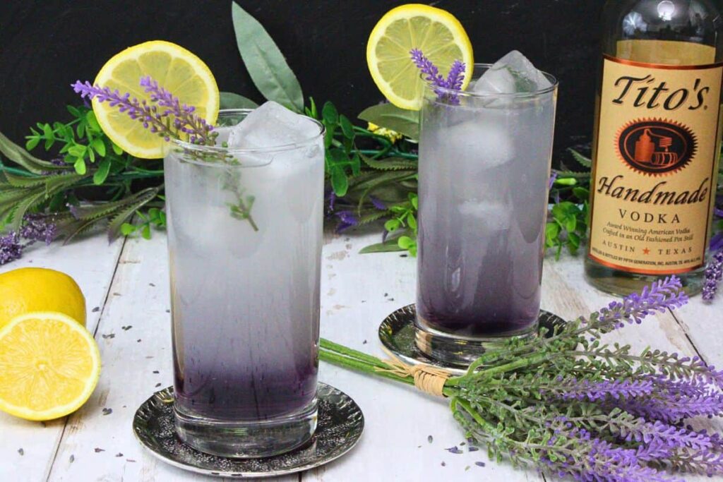 two lavender vodka lemonade cocktails garnished with lavender sprig and lemon slice surrounded by flowers