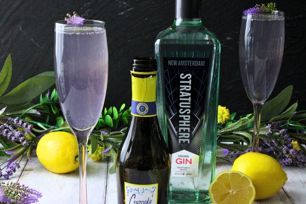 lavender french 75 next to champagne and gin bottles with fresh lemon and flowers
