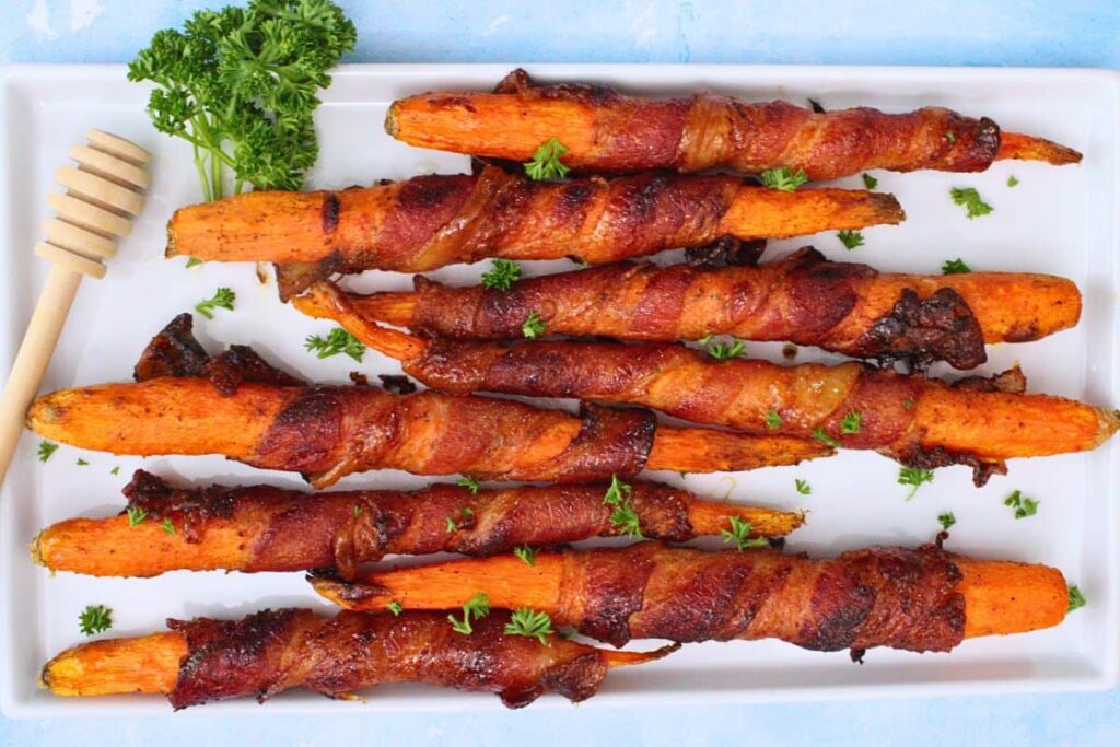 overhead view of air fryer bacon wrapped carrots on a white platter with fresh parsley