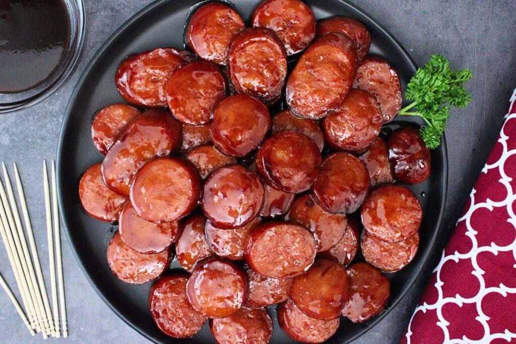 overhead view of bbq glazed kielbasa bites on a black plate garnished with parsley