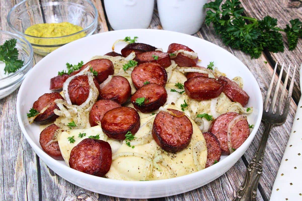 shallow bowl of kielbasa and pierogies with onions and parsley on rustic wooden table