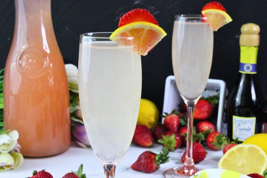 closeup of pink lemonade mimosa in champagne flute with lemon and strawberry garnish