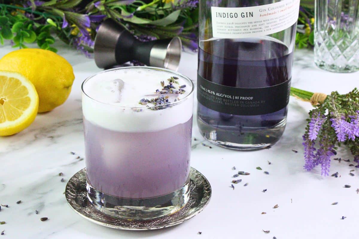 lavender gin sour garnished with lavender sprig next to gin bottle and fresh fruit