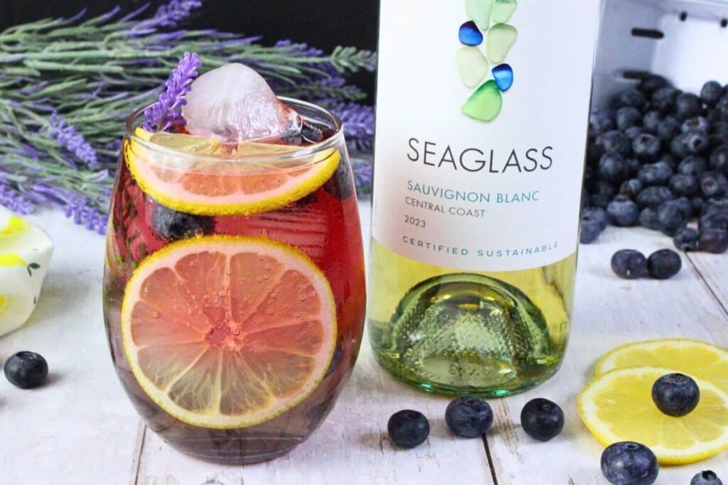 lavender sangria in stemless wine glass filled with fresh fruit next to wine bottle
