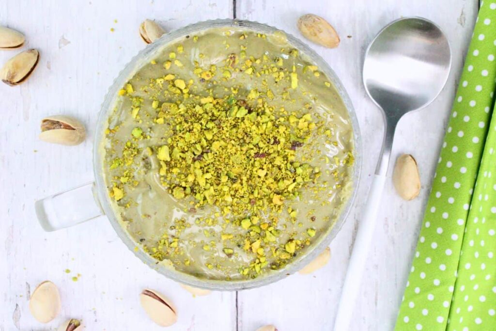 overhead view of pistachio mug cake with crushed nuts on top sitting on a wooden counter