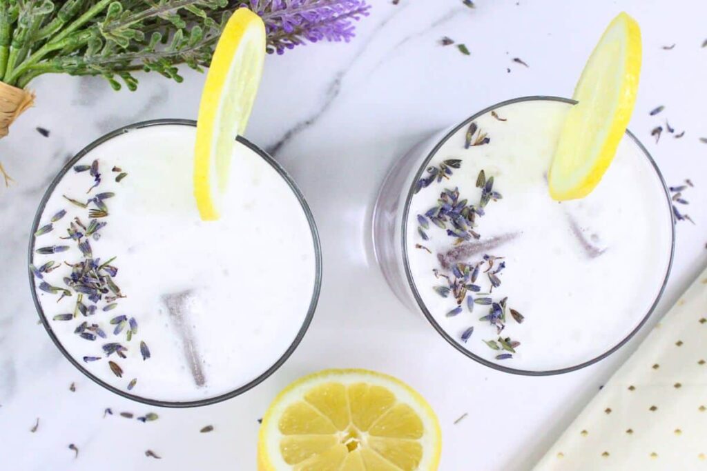 overhead view of two lavender gin sour drinks with lavender and lemon on marble counter