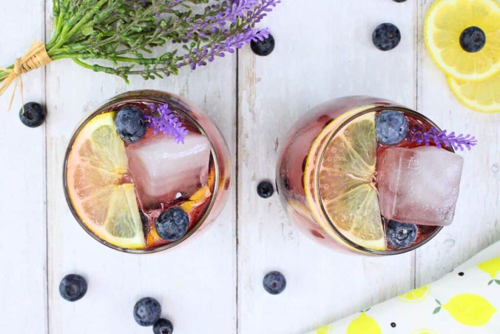 overhead view of two lavender sangria cocktails with fresh lavender lemon and blueberries on white wooden table