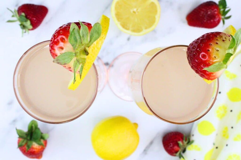 overhead view of two pink lemonade mimosa cocktails with fresh strawberries and lemon