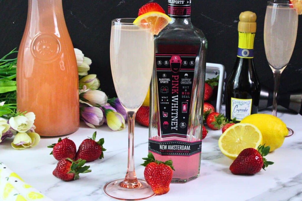 pink lemonade mimosa in champagne flute with fruit garnish next to pink whitney bottle