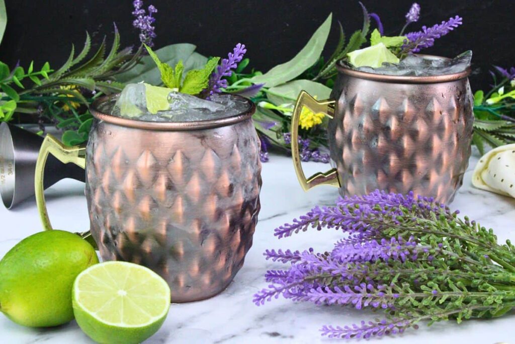 two lavender mules in copper mugs with crushed ice, lime, and lavender amidst fresh fruit and flowers