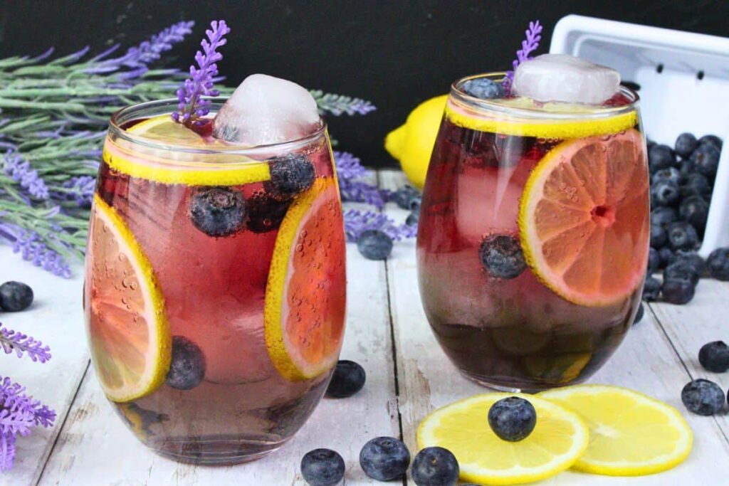 two lavender sangria drinks in stemless wine glasses filled with fresh lemon and blueberries