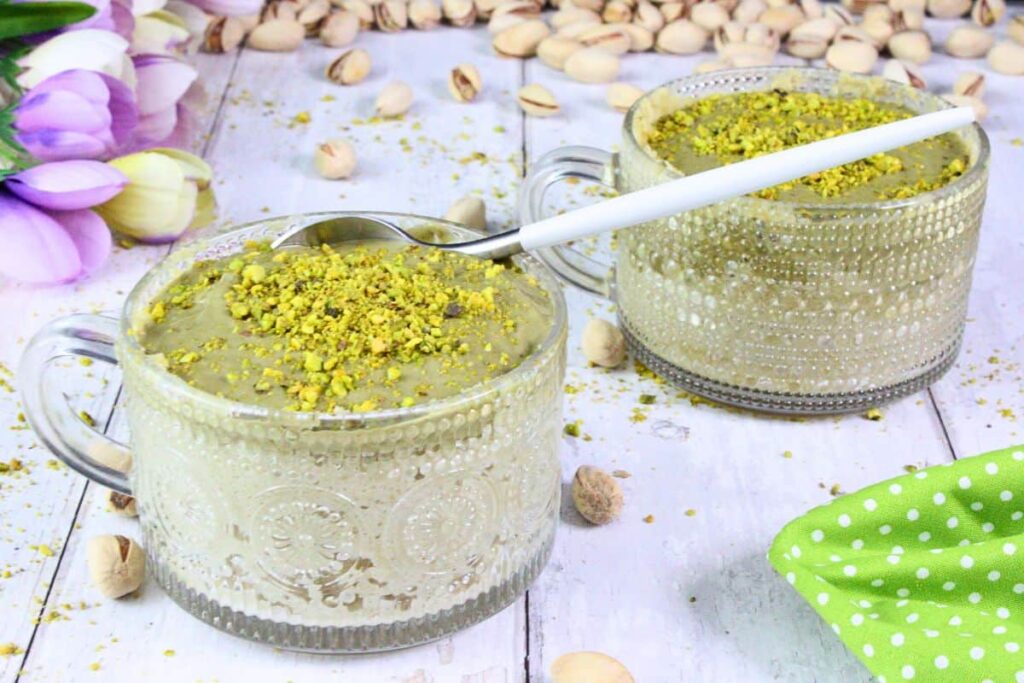 two pistachio mug cakes with crushed nuts on top and a spoon sticking out of one