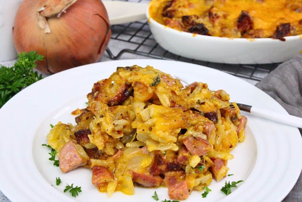 air fryer kielbasa casserole piled up on a white plate with the casserole dish in the back