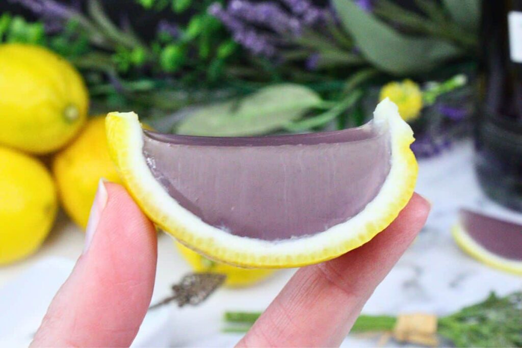 holding up a lavender lemonade jello shot fit inside a lemon rind