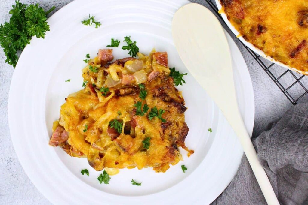 overhead view of cheesy kielbasa casserole on a plate garnished with parsley next to a wooden spoon