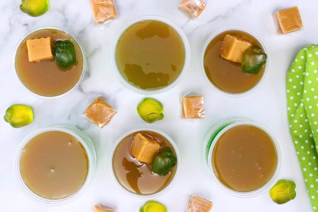 overhead view of several caramel apple jello shots with additional caramel and apple candy