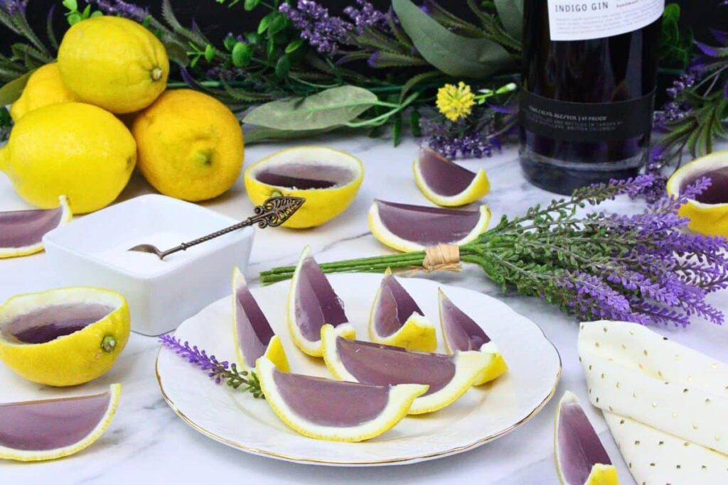 plate of lavender lemonade jello shots in lemon rinds amidst fresh lemons and flowers