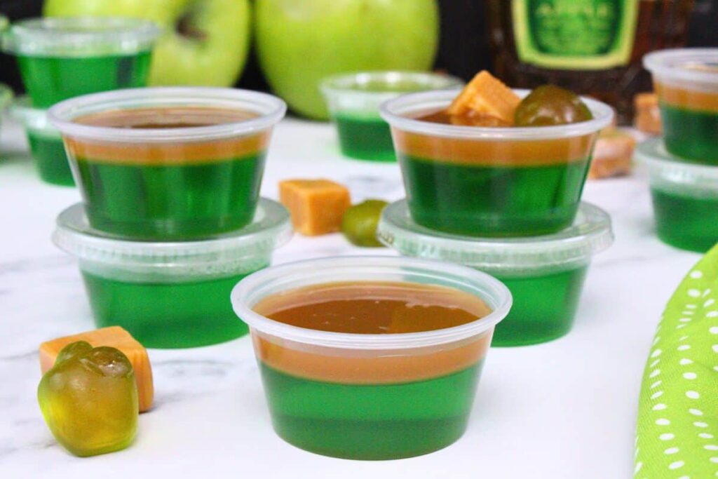 several dual layer caramel apple jello shots stacked on each other with fresh apples in the back