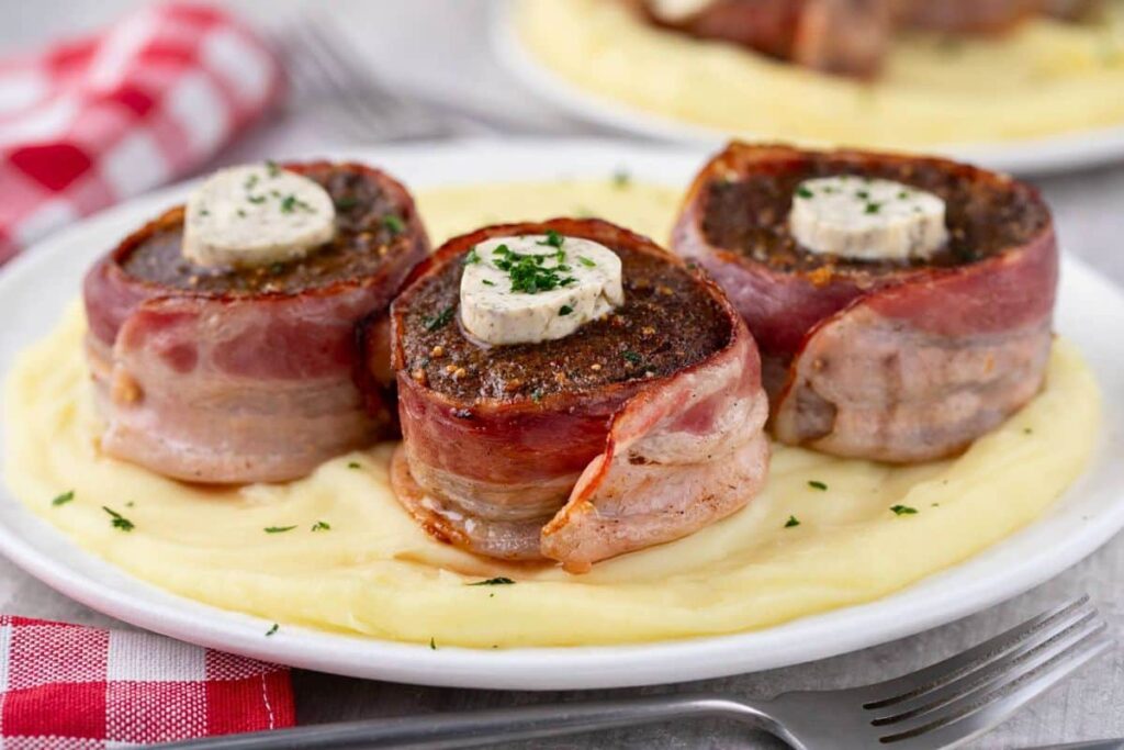 three air fryer bacon wrapped filet on a plate of mashed potatoes topped with herb butter