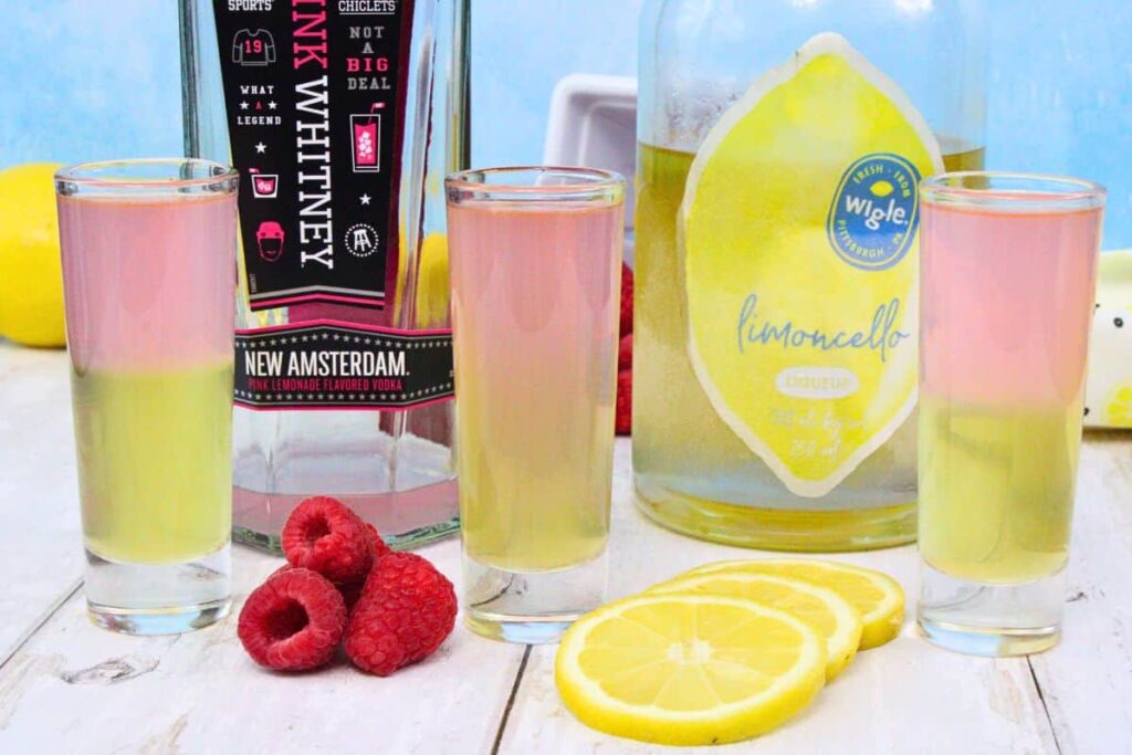 three layered pink whitney shots with pink whitney and limoncello bottles between thrm