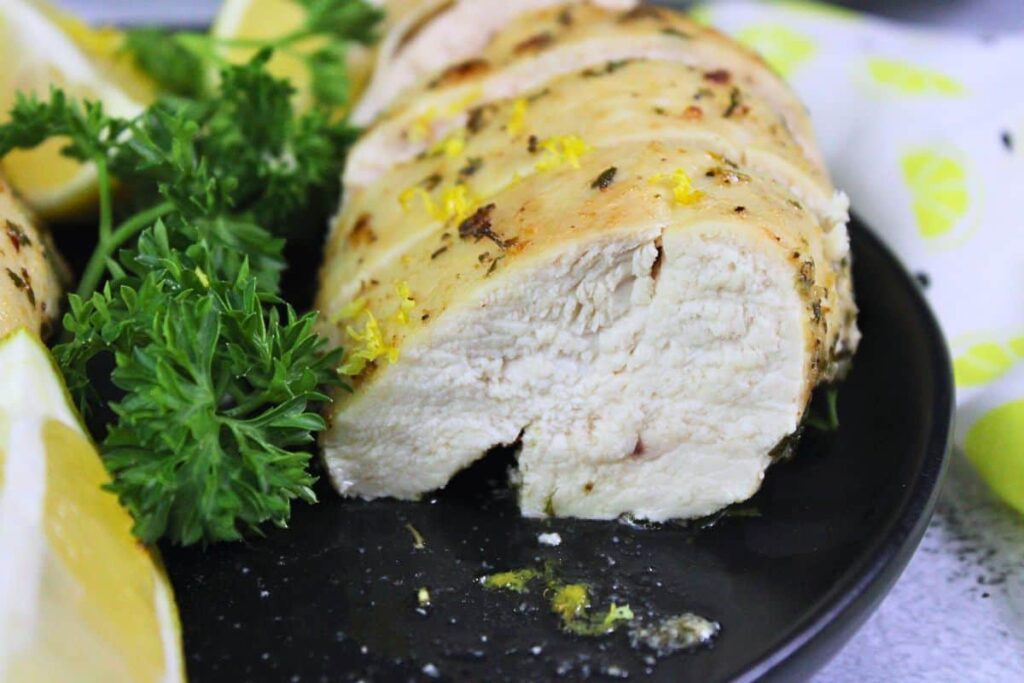 closeup view of a juicy slice of air fryer lemon garlic chicken breast next to parsley and lemon