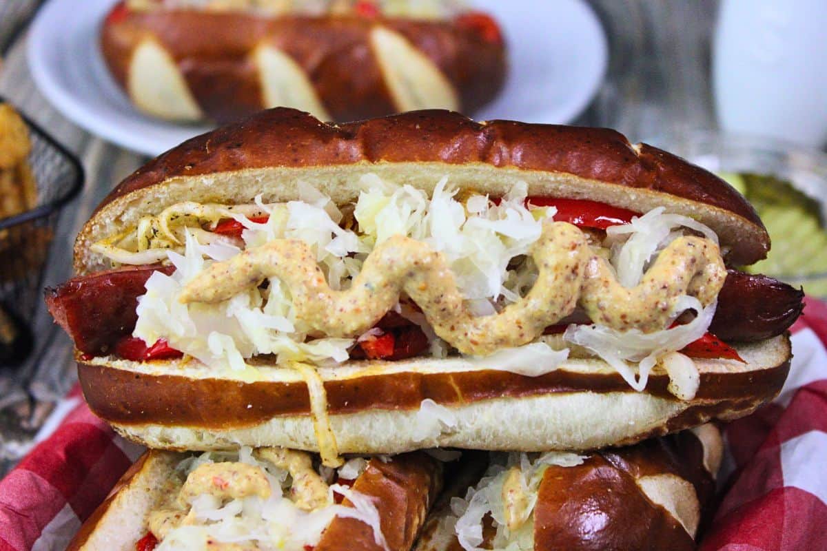 closeup view of sideways kielbasa sandwich on a pretzel bun with mustard, sauerkraut, peppers, and onions