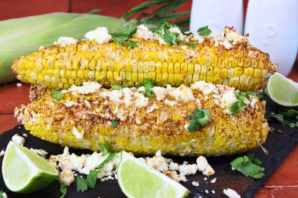 ears of mexican street corn sideways with mayo crema sauce and cojita cheese plus fresh lime wedges