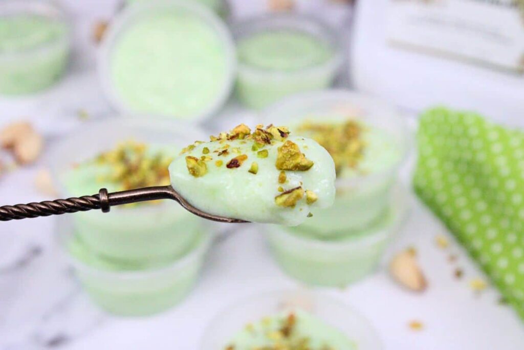 holding up a small spoon with pistachio pudding and crumbled nuts on top