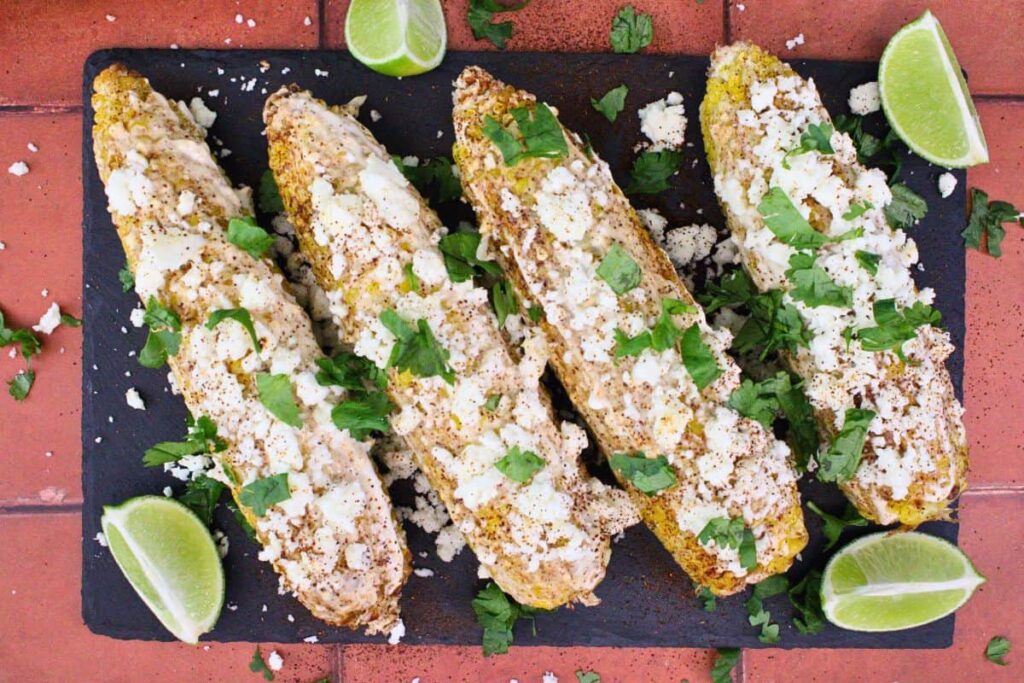 overhead view of air fryer elote with cojita cheese and cilantro on a black slate
