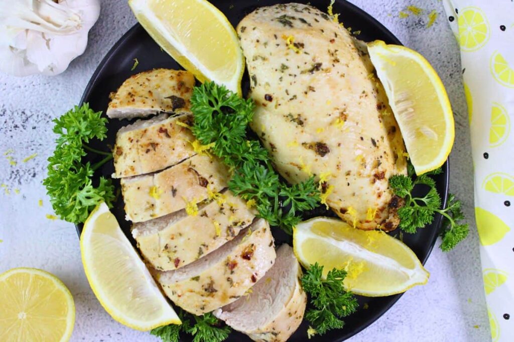 overhead view of two lemon garlic chicken breasts on a black plate garnished with lemon and parsley