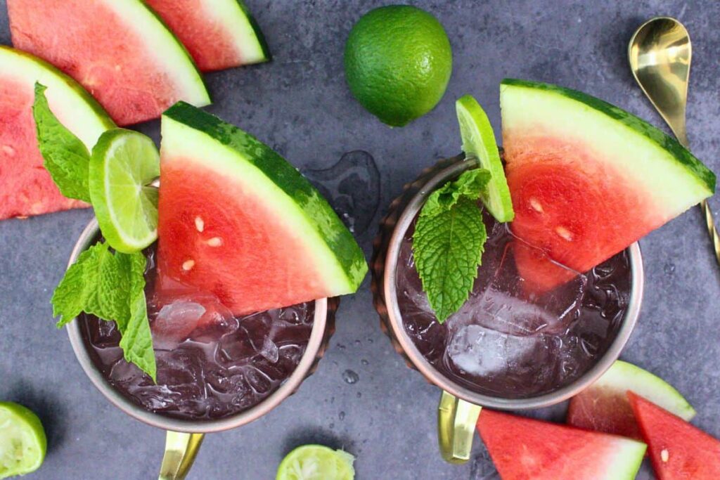 overhead view of two watermelon moscow mules with fresh watermelon, mint, and lime garnish