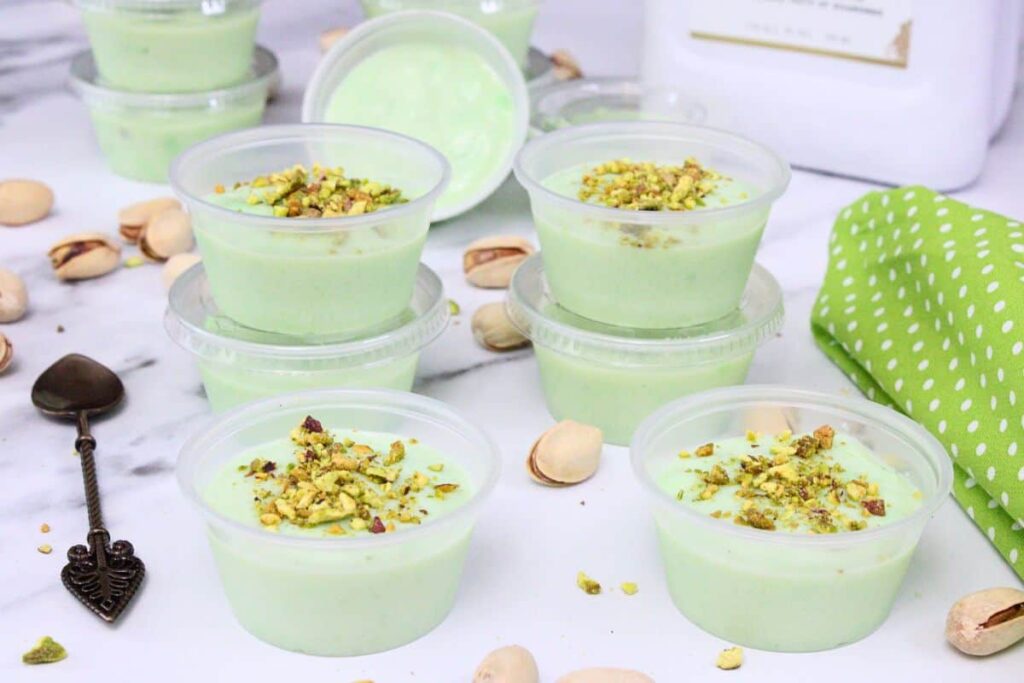 pistachio pudding shots spread across a marble counter with lots of crushed nuts