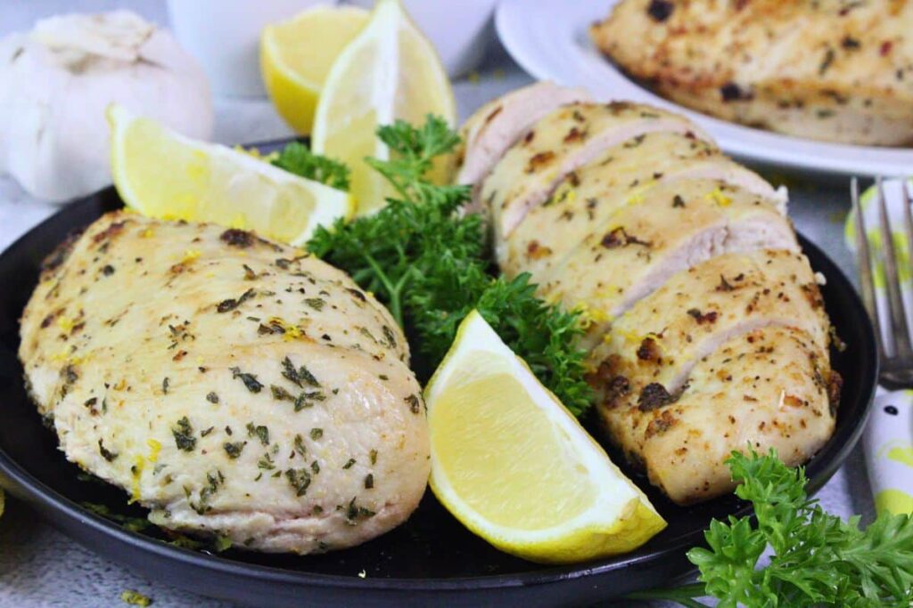 two lemon garlic chicken breasts one sliced and one whole garnished with lemon and parsley
