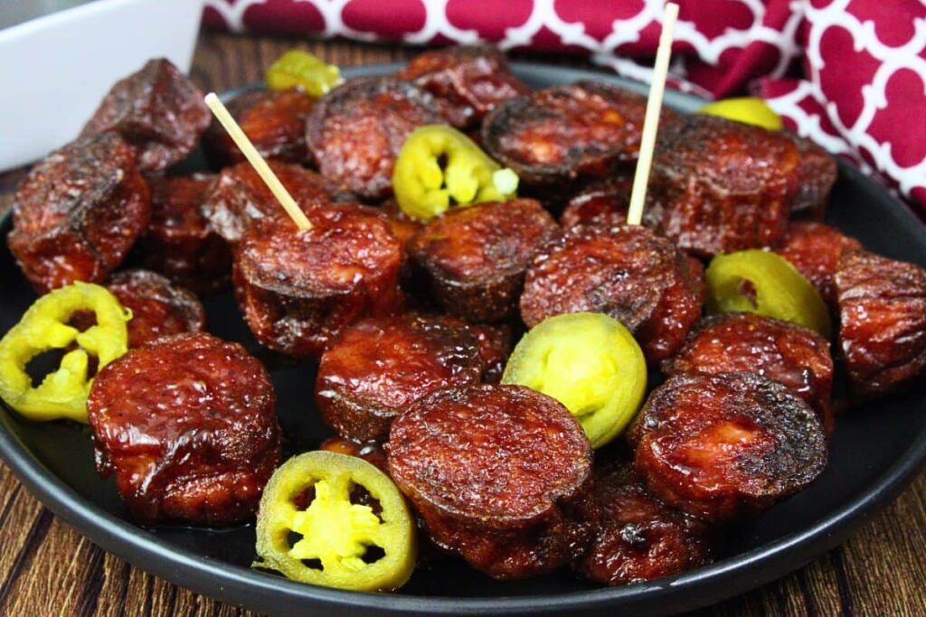 black plate with bbq kielbasa burnt ends with jalapenos scattered around