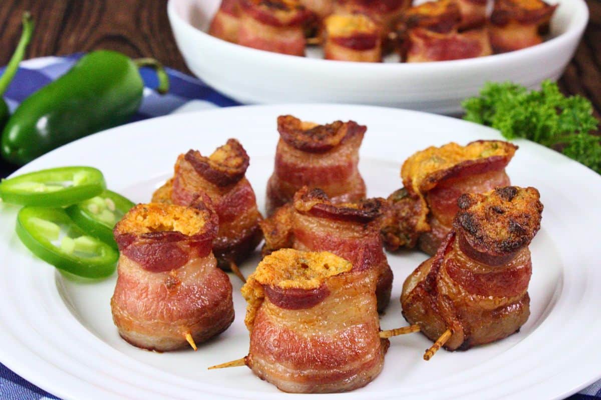plate of bacon wrapped pig shots on a plate with fresh jalapenos and more in the background