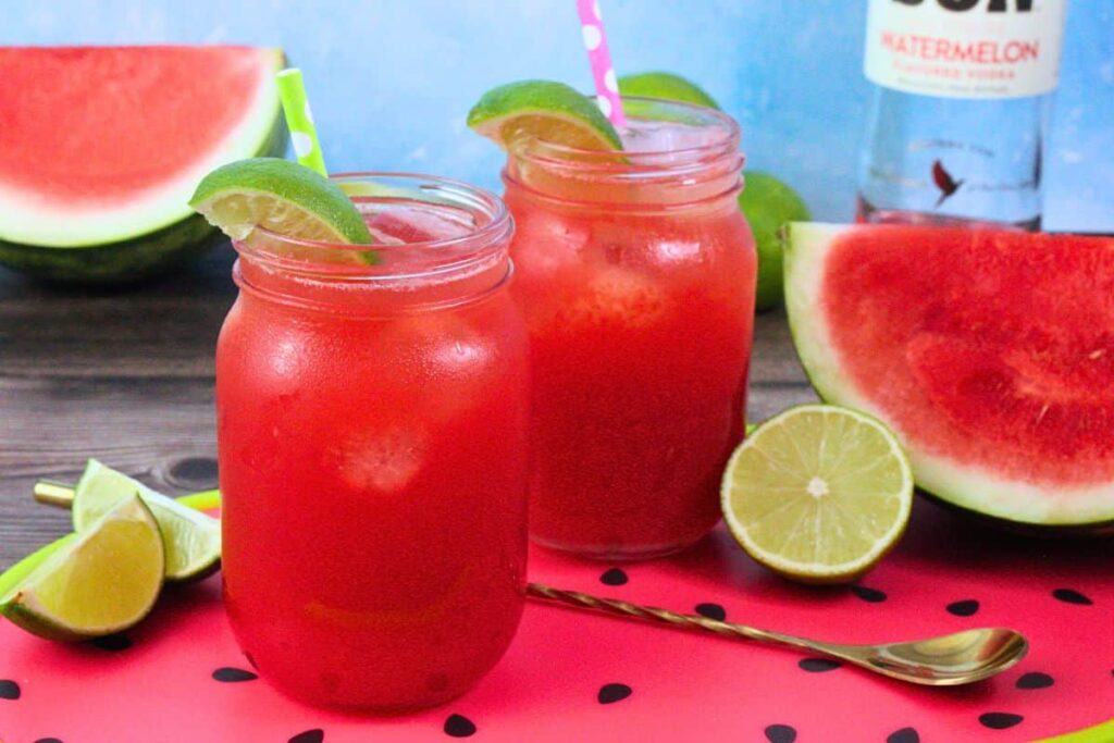 two watermelon limeade drinks on fruit serving platter next to more fresh fruit