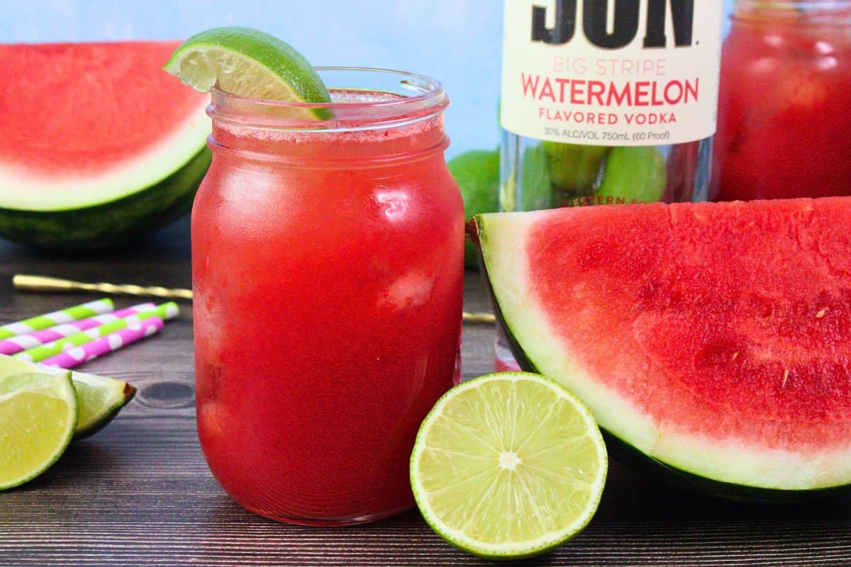 watermelon limeade drink garnished with lime wedge next to cut fresh fruit