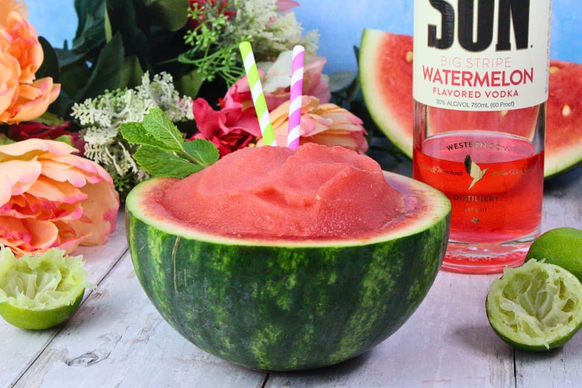 watermelon slushie served in watermelon rind next to fresh limes and vodka bottle