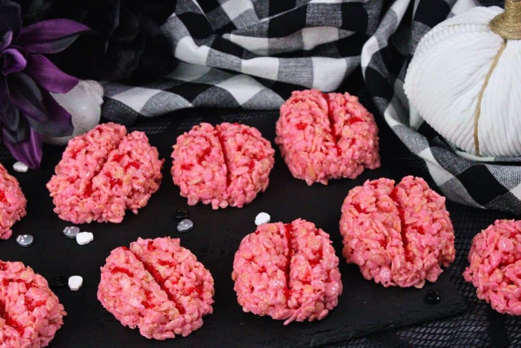 angled view of brain rice krispie treats on slate with halloween color decorations and white pumpkin