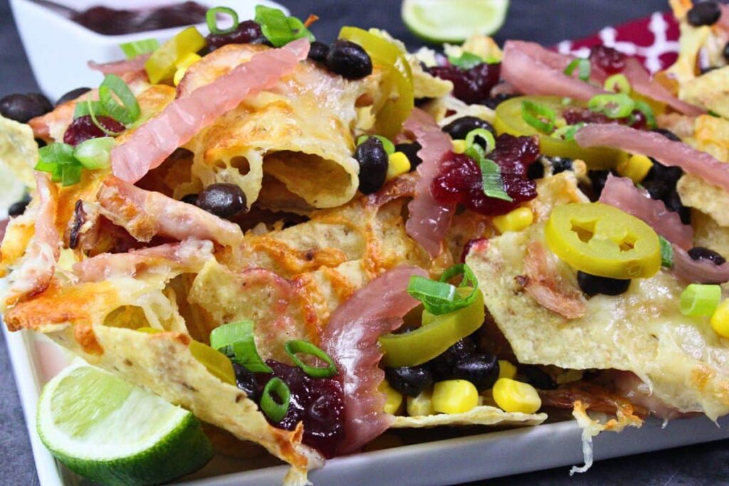 closeup view of air fryer turkey nachos on a platter with loaded toppings like jalapenos, pickled red onions, corn, black beans, and cranberry relish