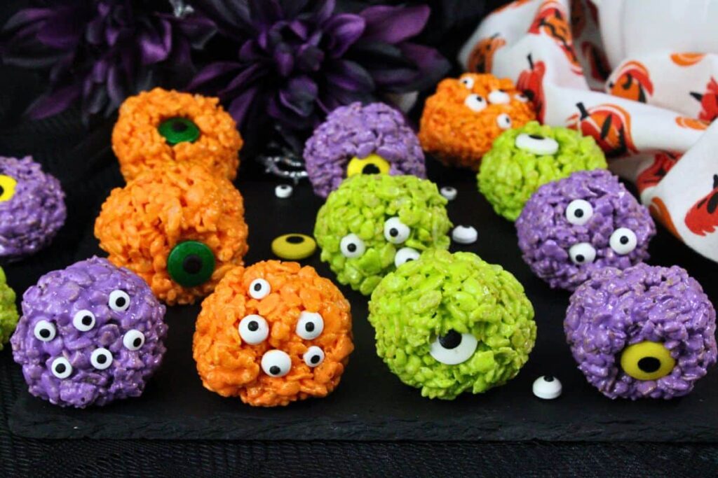 orange, green, and purple monster rice krispie treats with assorted candy eyes in dark halloween setting